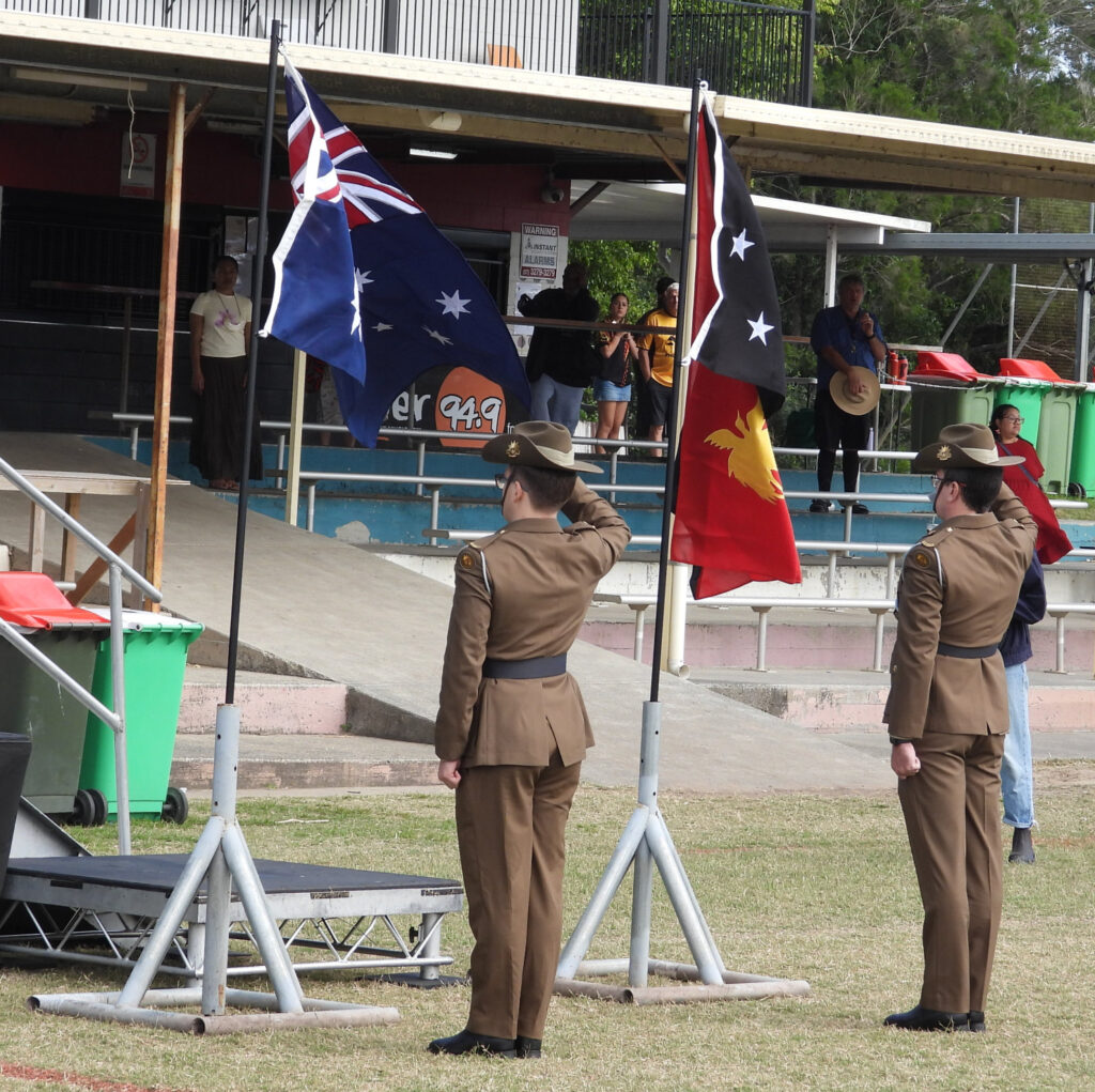 Soldiers saluting Australian and Papua New Guinea flags.